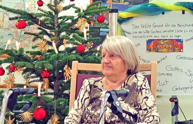 Ältere Frau neben geschmücktem Weihnachtsbaum mit Rollator