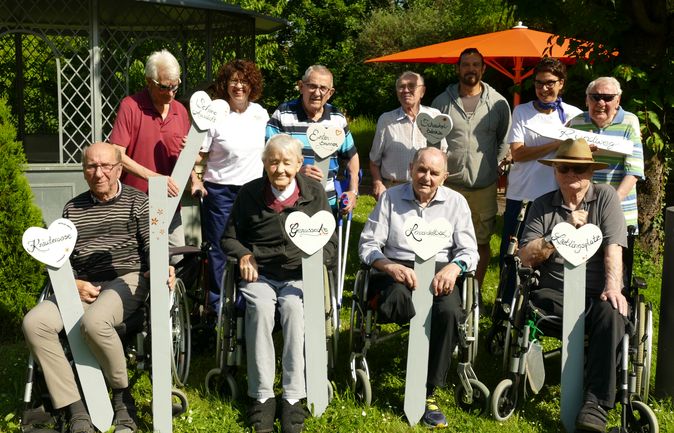 Bewohner und Betreuungs- sowie Haustechnikmitarbeitende halten beschriftete Stelen im Garten