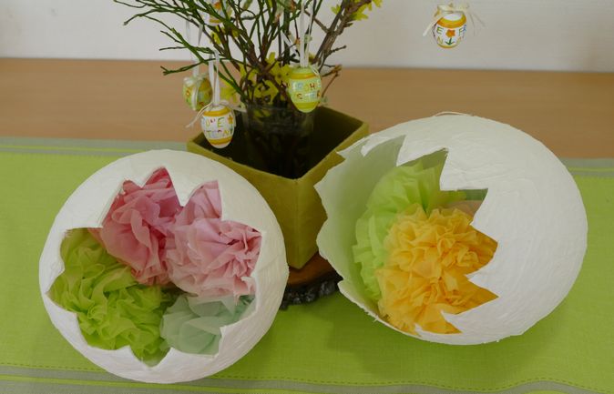 Aufgebrochene Papier-Eier mit Seidenblüten und hängenden Ostereiern
