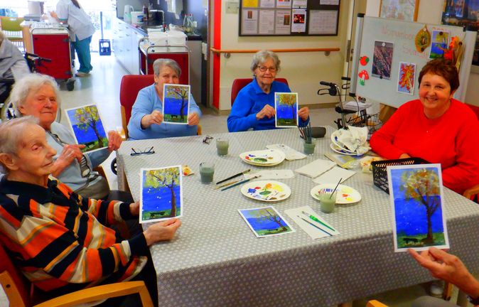 Seniorinnen in einer Gruppe zeigen selbstgemalte Baumbilder beim Malangebot