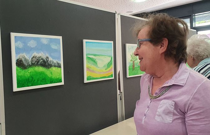 Ältere Frau betrachtet sommerliche Landschaftsgemälde in einer Kunstausstellung