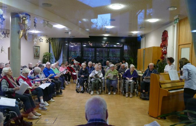 Ältere Menschen, teils in Rollstühlen, singen mit Liedblättern begleitet am Klavier