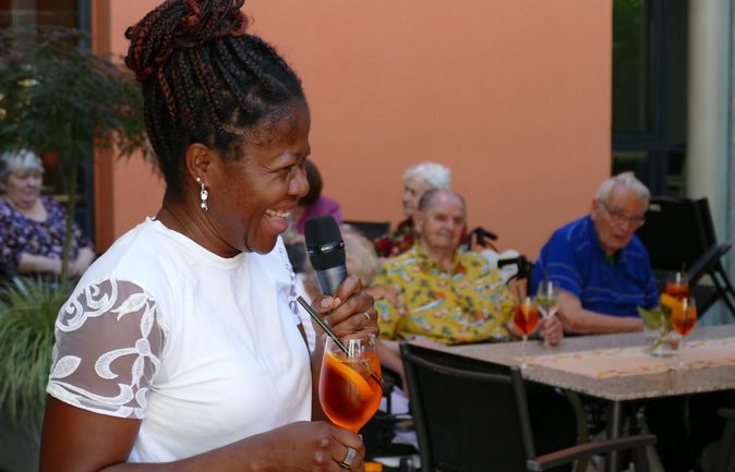 Lächelnde Frau mit Mikrofon und Aperol Spritz beim Sommerfest